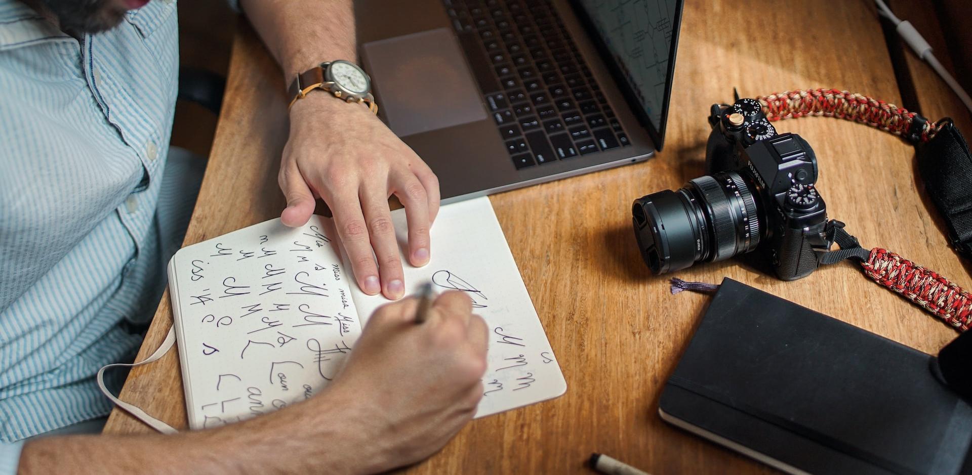 man writing on paper in front of DSLR